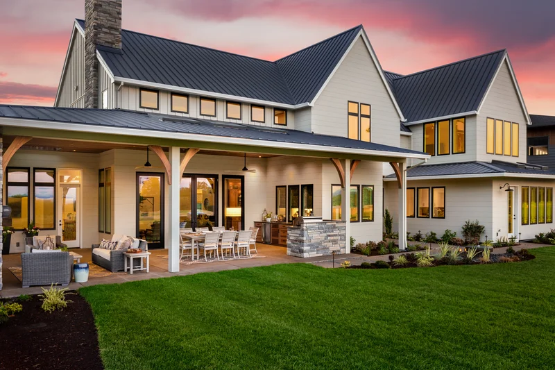 Modern white farmhouse exterior with black metal roof at sunset